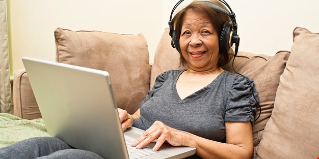 Kvinna med hörlurar framför en laptop. Fotografi